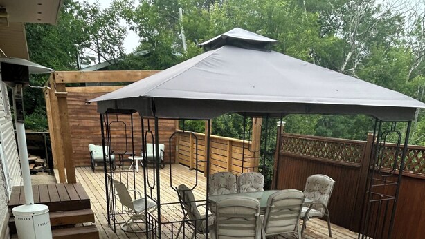 Una terraza de madera con un patio cubierto, mobiliario exterior y una parrilla.