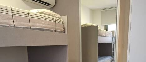 A bunk bed room with a desk and chair, an air conditioning unit, and a mirror.