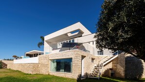 Ein modernes Haus mit Natursteinfassade, großen Fenstern und einer Treppe, die zu einem Balkon führt.