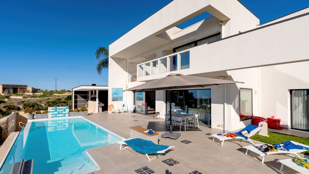 Ein modernes Haus mit Schwimmbad, Sitzgelegenheiten im Freien und einer großen Terrassenfläche.