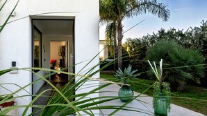 Ein modernes Haus mit weißer Fassade, einer sichtbaren Tür und einem Garten mit verschiedenen Pflanzen.