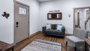 A modern entryway with a gray door, a welcome sign, a gray sofa with patterned cushions, and a patterned rug.