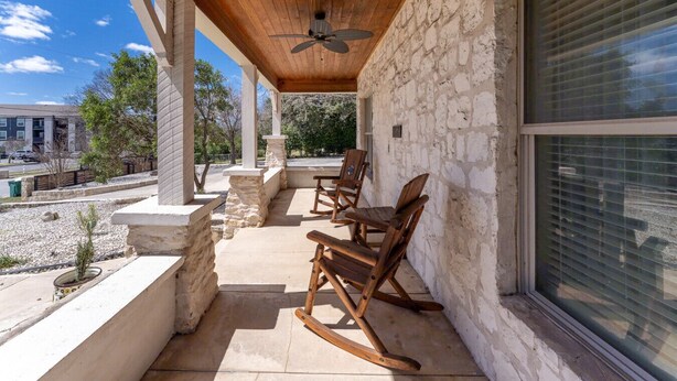 A covered patio with stone walls, wooden rocking chairs, and a ceiling fan.