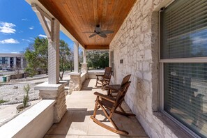 Une terrasse couverte avec des murs en pierre, des fauteuils à bascule en bois et un ventilateur de plafond.