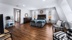 A bedroom with a bed, bedside tables, a TV, a microwave, and a chair.