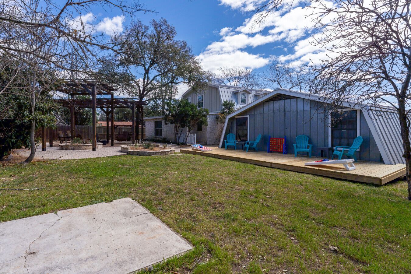 Un patio trasero con un porche de madera, una casita con terraza y un césped.