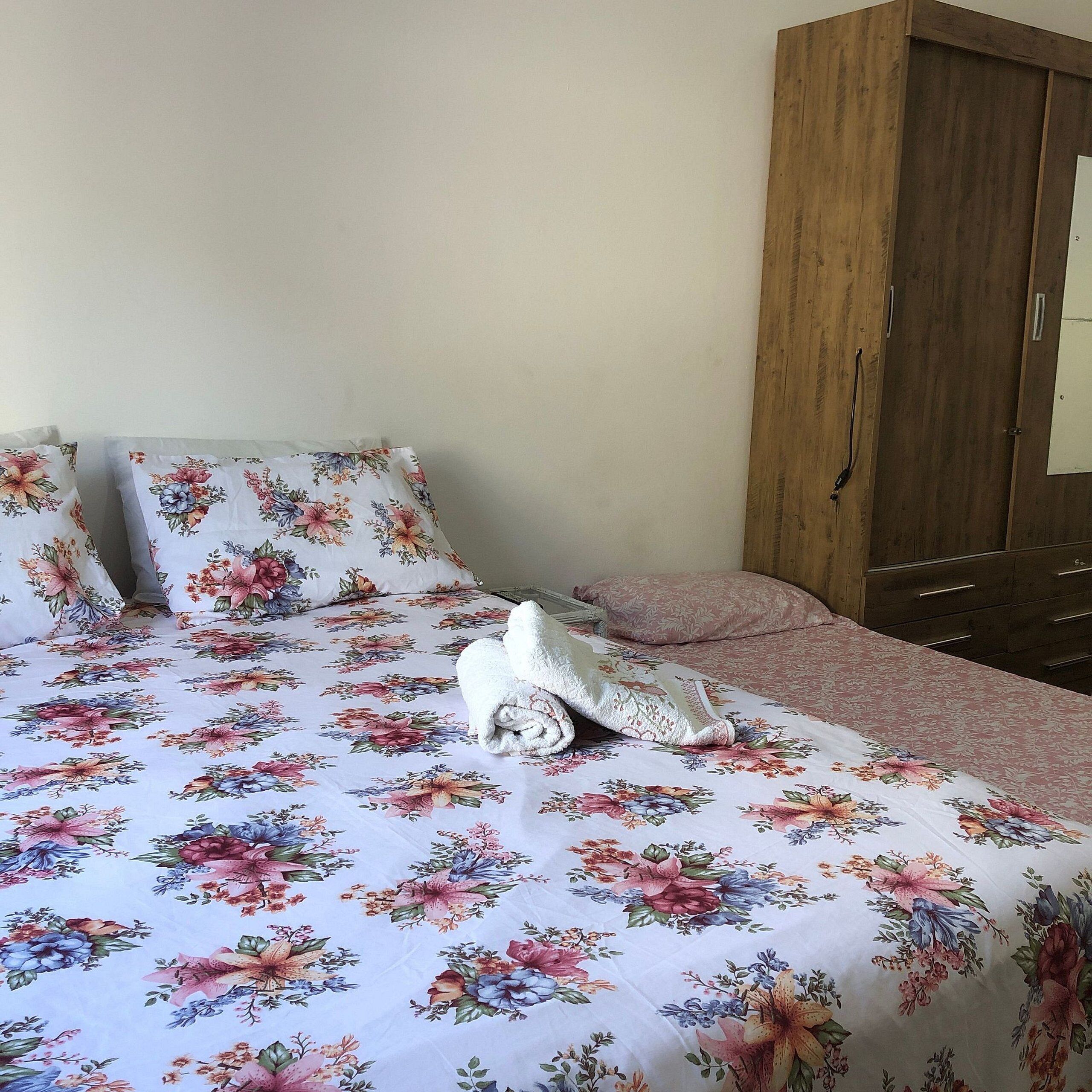 A bed with floral bedding, a rolled towel, and a wooden wardrobe in a room.