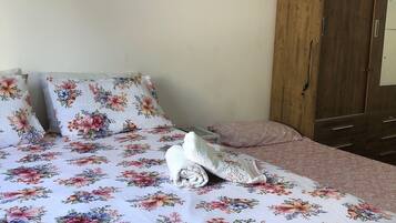 A bed with floral bedding, a rolled towel, and a wooden wardrobe in a room.