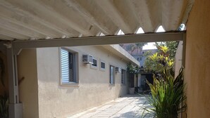 Ένα στενό σοκάκι με πλακόστρωτο δάπεδο, ένας σκεπαστός χώρος με λευκό ταβάνι και γλάστρες με φυτά.