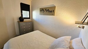 Un dormitorio con una cama, un aparador, una obra de arte colgada en la pared y una ventana con persiana.