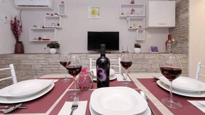 A dining area with a table set for two, a bottle of wine, and glasses of red wine. There is a flat-screen TV mounted on the wall above the table.