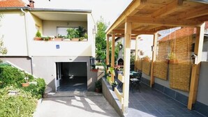 A covered outdoor area with a wooden pergola, a barbecue grill, and a small seating area with a table and chairs.