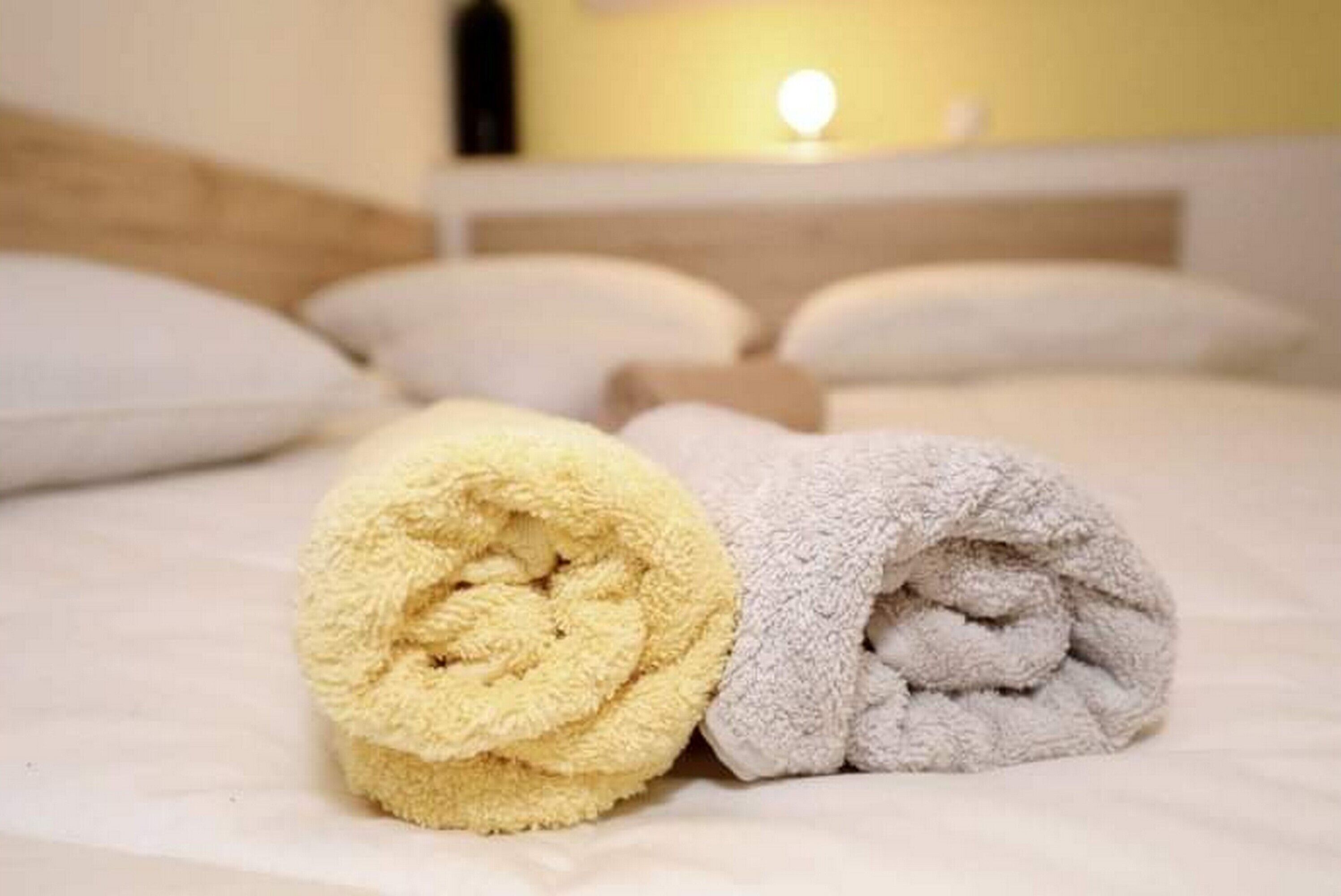 Ein ordentlich bezogenes Bett mit aufgerollten Handtüchern in Gelb und Grau.