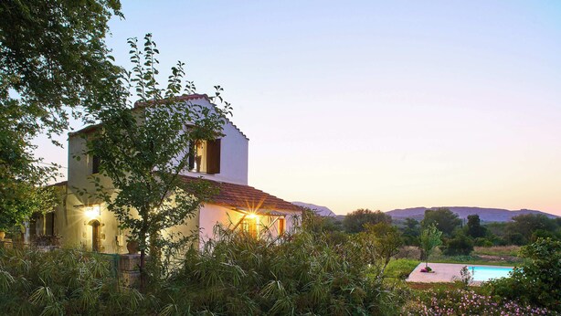 A white building with a red roof, surrounded by lush greenery and a swimming pool.