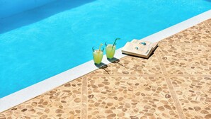 A poolside area with a tiled floor, two glasses of a green beverage, and a menu on the right.