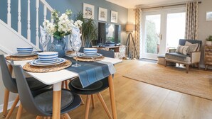 A dining area with a table set for four, a sofa, and a television in the background. - Breeze Cottage (Falmouth)