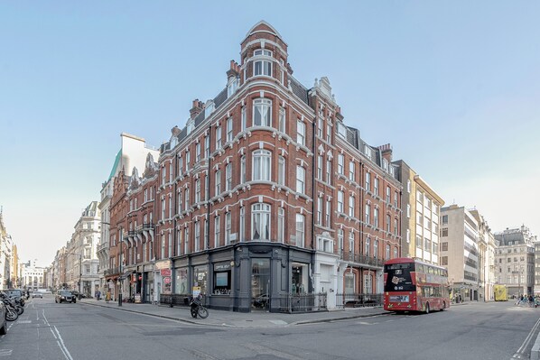 A corner building with a black storefront and a red double-decker bus in front.