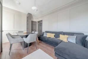 Una sala moderna con un sofá gris oscuro, dos sillas grises, una mesa de comedor y un tapete blanco.