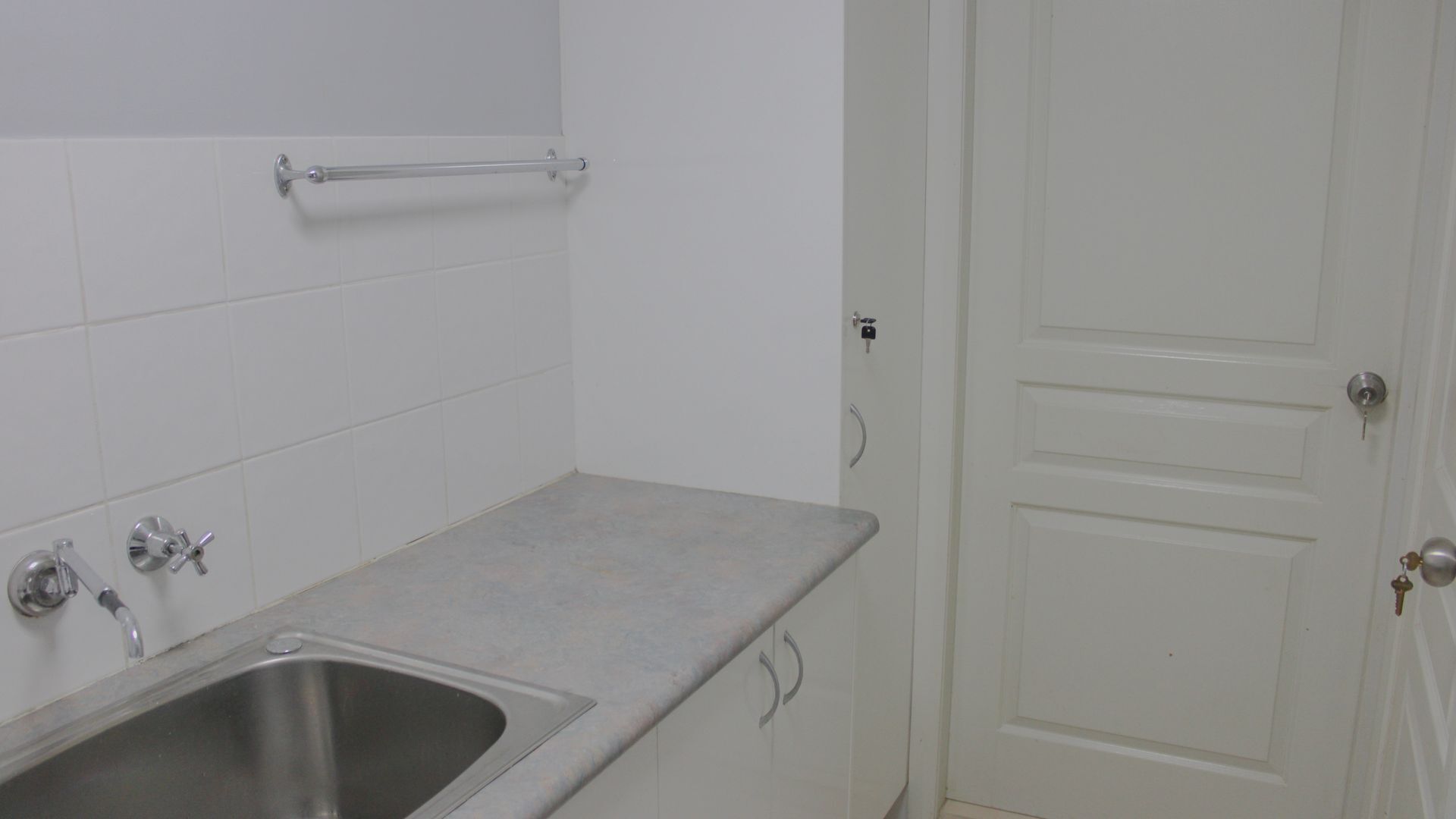 A bathroom with a stainless steel sink, a towel rack, and a white door.