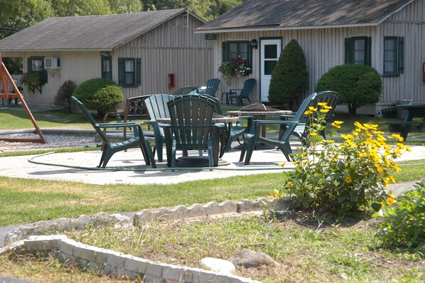 A patio area with outdoor furniture, a swing set, and a small garden with yellow flowers. - Lincoln Log Colony (Lake George)