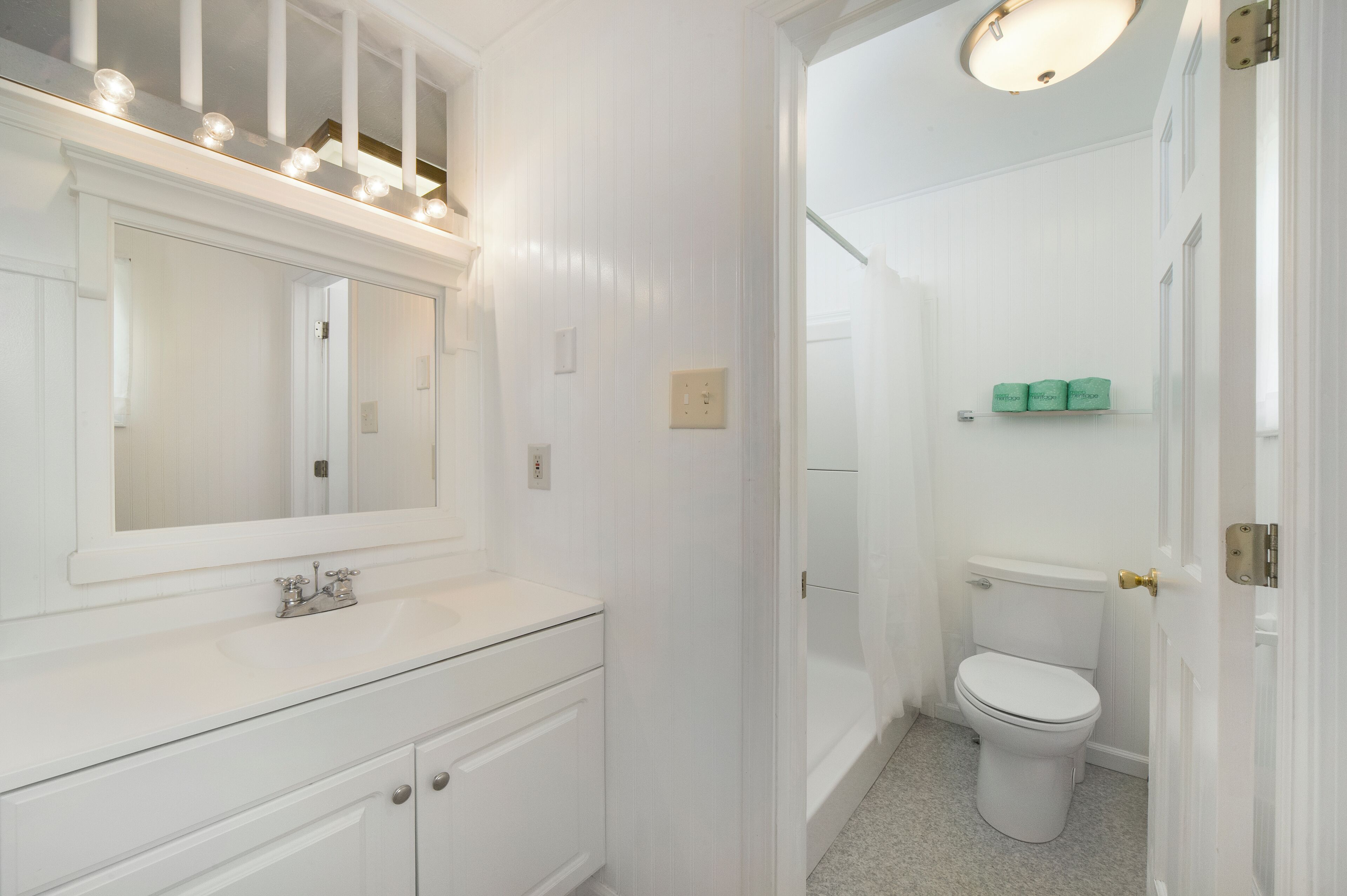 Een badkamer met een wit wastafelmeubel, een spiegel met verlichting, een toilet en een douche.