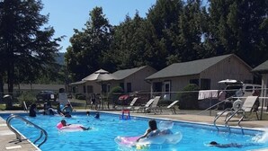 Una piscina con flotadores inflables, rodeada de sillas de descanso y una valla.