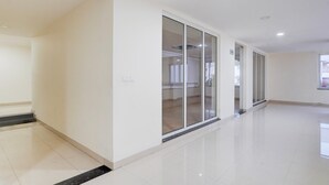Un pasillo amplio y luminoso con suelo de baldosas brillantes, que conduce a una habitación con puertas de vidrio grandes.