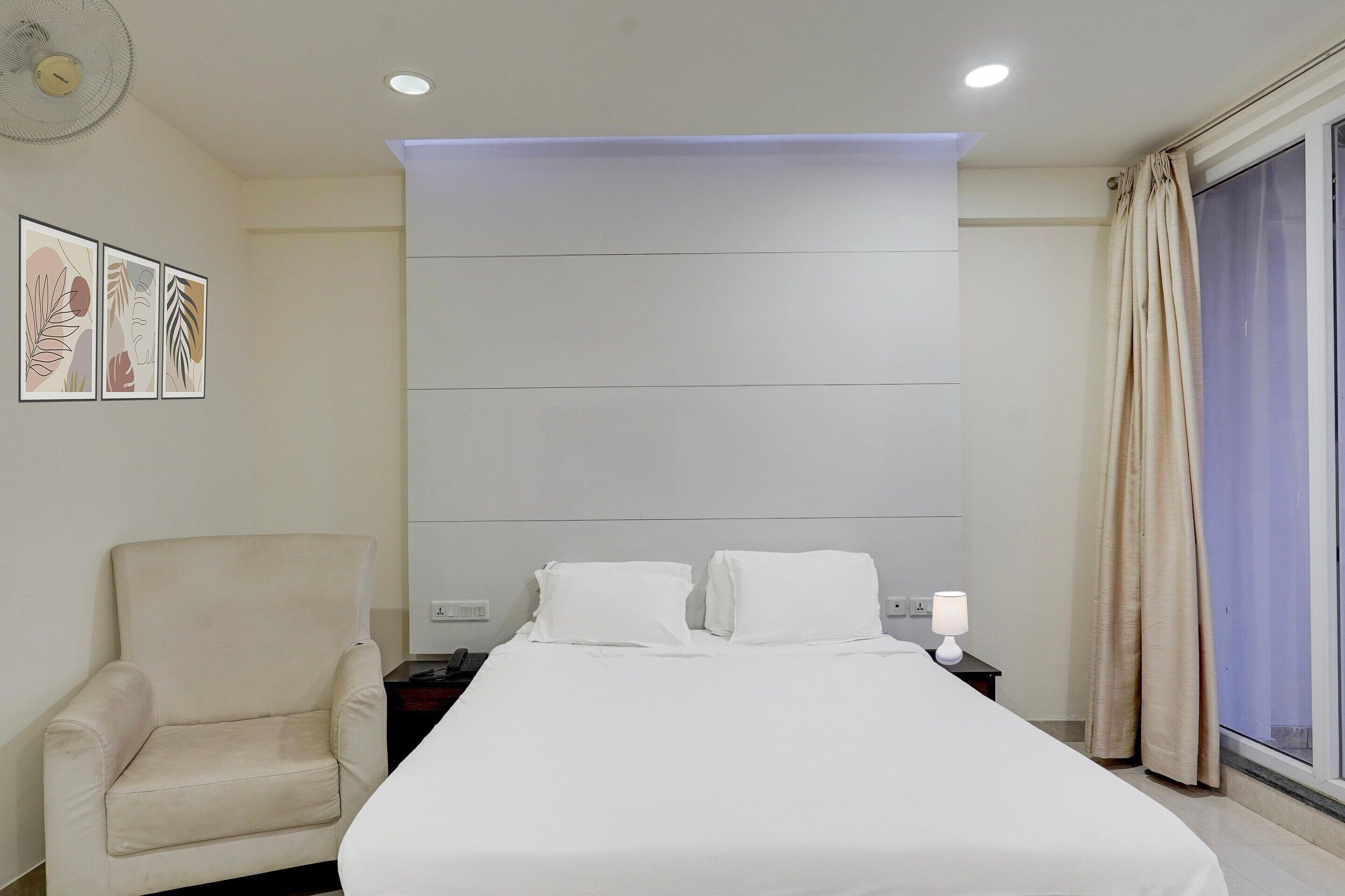 A hotel room with a bed, a chair, a nightstand, a lamp, and a window with curtains.