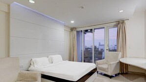 Una habitación de hotel moderna con una cama grande, un área de descanso y vistas a la ciudad a través de amplios ventanales.