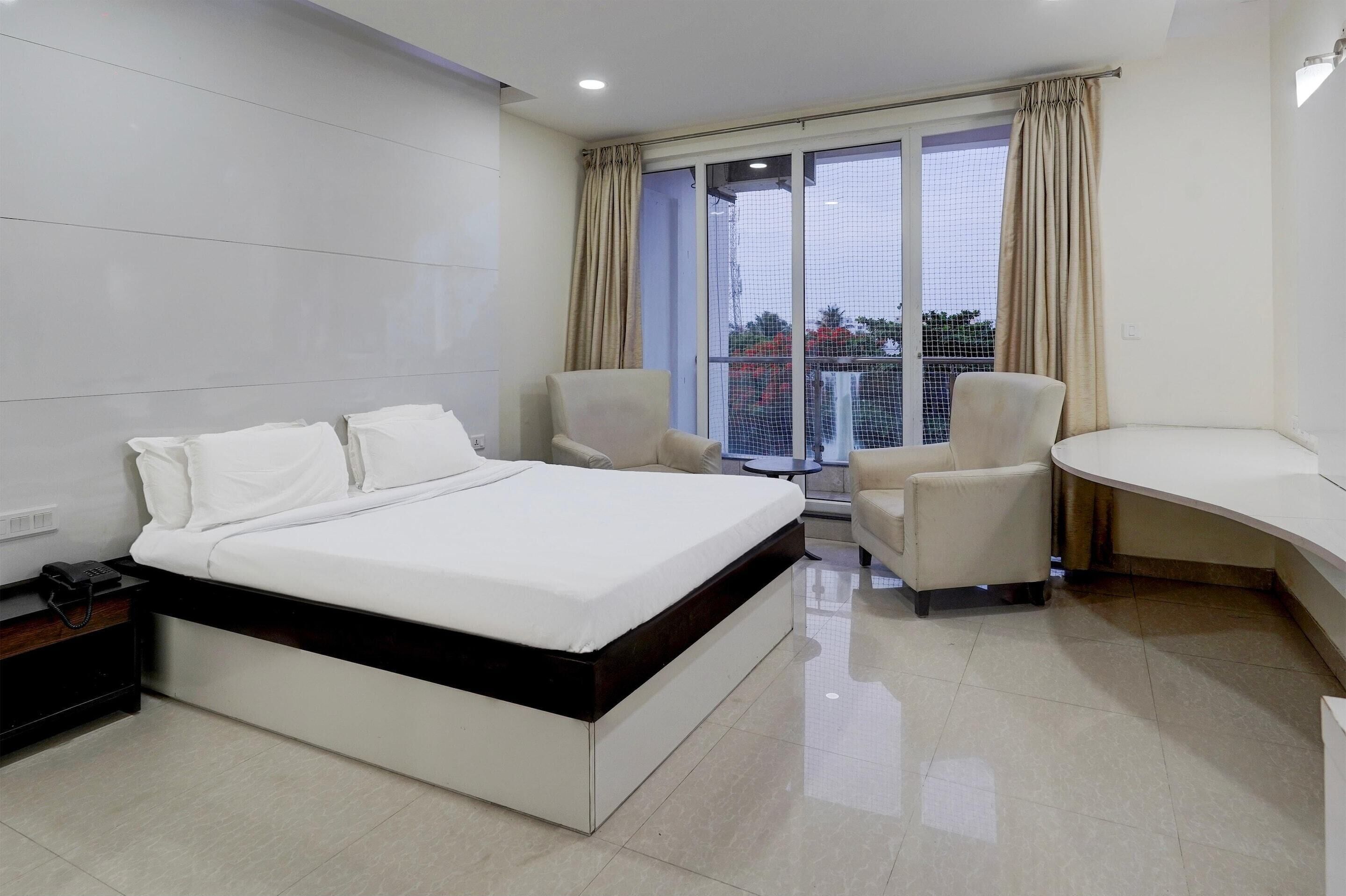 Una habitación de hotel moderna con una cama grande, dos sillones, un escritorio curvo y un balcón con vistas.