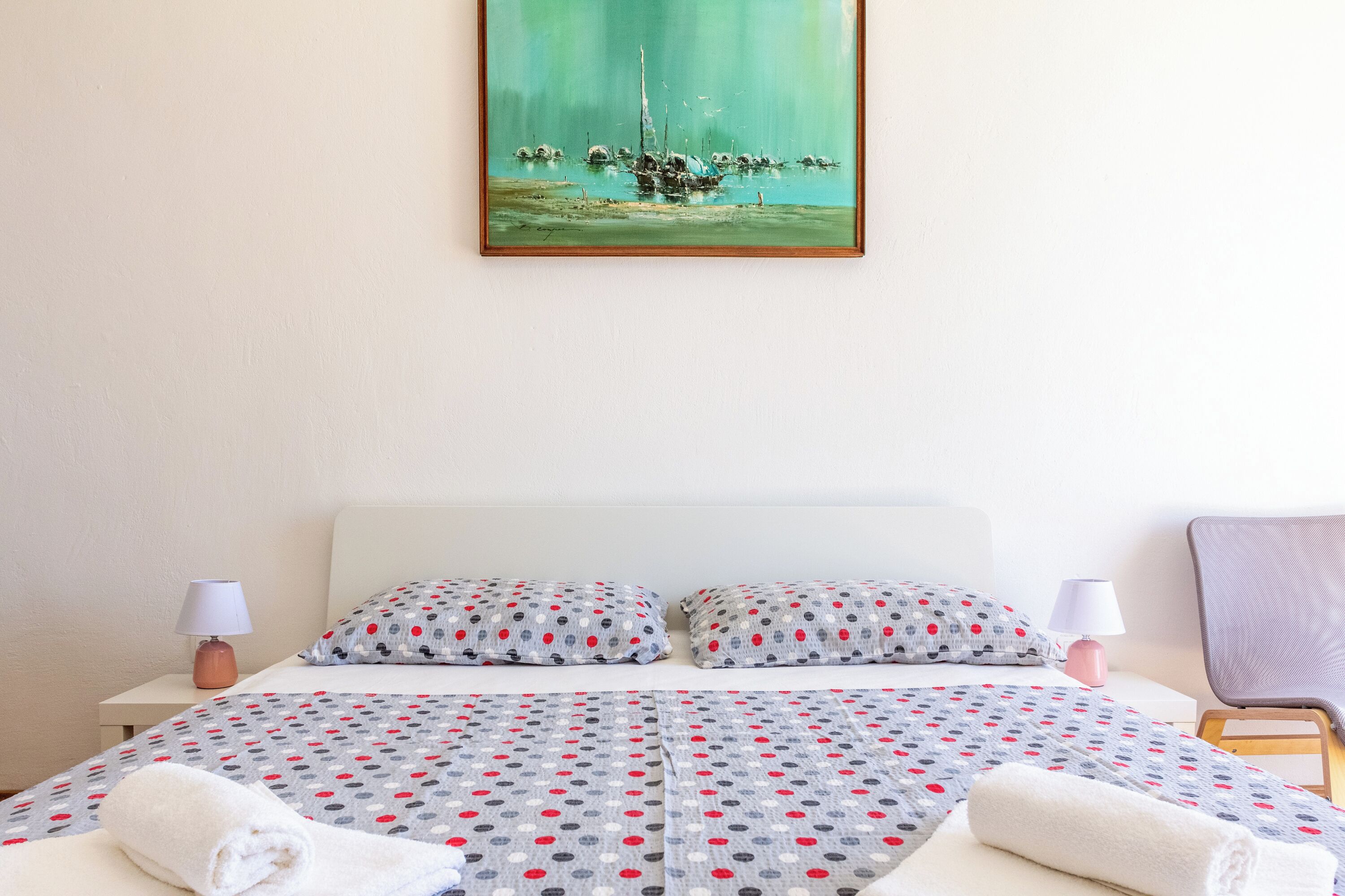 Un lit bien fait, recouvert d’une couvre-lit à motifs, avec deux oreillers et deux lampes de chevet.