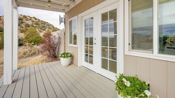 Une véranda couverte avec une terrasse en bois, des portes blanches et des plantes en pot.