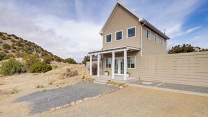 Une maison à deux étages avec un porche couvert, une allée en gravier et une colline en arrière-plan.