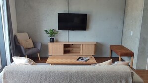 En moderne stue med en stor grå sofa, et træbord, et fladskærms-tv monteret på væggen, et lille træ-sidetabel og en grå lænestol.
