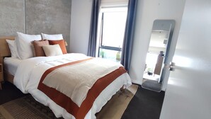 Et moderne hotelværelse med en stor seng, et trænatbord, en senelampe og udsigt til det fri gennem et vindue.