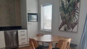 Et moderne køkken med hvide skabe, opvaskemaskine og et vindue med persienner.