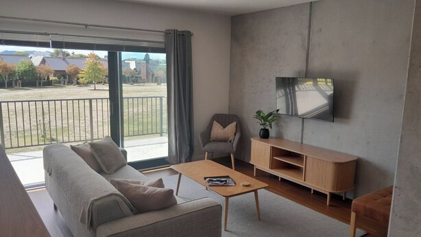 En moderne stue med sofa, sofabord, fjernsyn og udsigt til en altan.