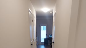 Ein schmaler Korridor mit hellen Wänden und Holzboden, der zu einem Zimmer mit Schreibtisch und Fenster führt.