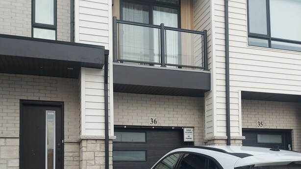 Ein weißer SUV vor einem zweistöckigen Gebäude mit nummerierten Türen, einem sichtbaren Balkon und einem Schotterweg.