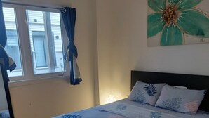 Ein Schlafzimmer mit Bett, einem Fenster mit Vorhängen, einem Bild an der Wand und einem Teppich.