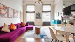 A modern living room with a purple sofa, a wooden coffee table, and a dining area with a white table and chairs. - 3bedroom Design Gem in Kensington (London)