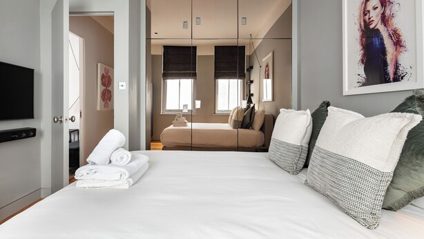 A modern hotel room with a large bed, a wardrobe, a television, and a painting on the wall. - 3bedroom Design Gem in Kensington (London)