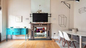 A modern living room with a fireplace, teal-colored desk, white chairs, and a dining table. - 3bedroom Design Gem in Kensington (London)