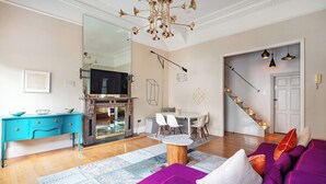 A modern living room with a purple sofa, wooden coffee table, and a large mirror. - 3bedroom Design Gem in Kensington (London)