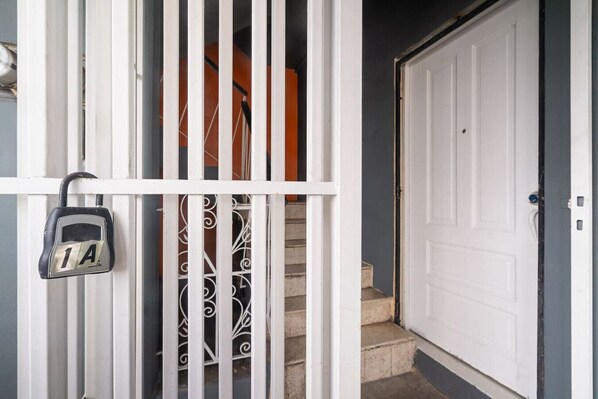 A white metal gate with a padlock, a staircase, and a white door.