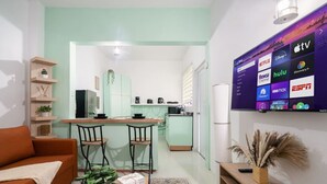 Un espacio habitable compacto con kitchenette, televisor que muestra varios servicios de streaming y una zona de estar acogedora con sofá y sillones.