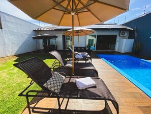 Un patio trasero con piscina, sillas de descanso y un área de terraza cubierta.