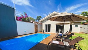 A backyard with a swimming pool, lounge chairs, and a covered patio area. - Casa com piscina 5 suites 1 quarto e AC (Foz do Iguaçu)