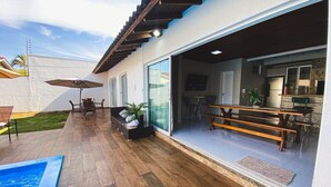 A modern patio with wooden flooring, a pool, and a dining area with outdoor furniture. - Casa com piscina 5 suites 1 quarto e AC (Foz do Iguaçu)