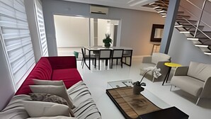 A modern living room with a red sofa, a coffee table, and a dining area with a white table and chairs. - Casa com piscina 5 suites 1 quarto e AC (Foz do Iguaçu)